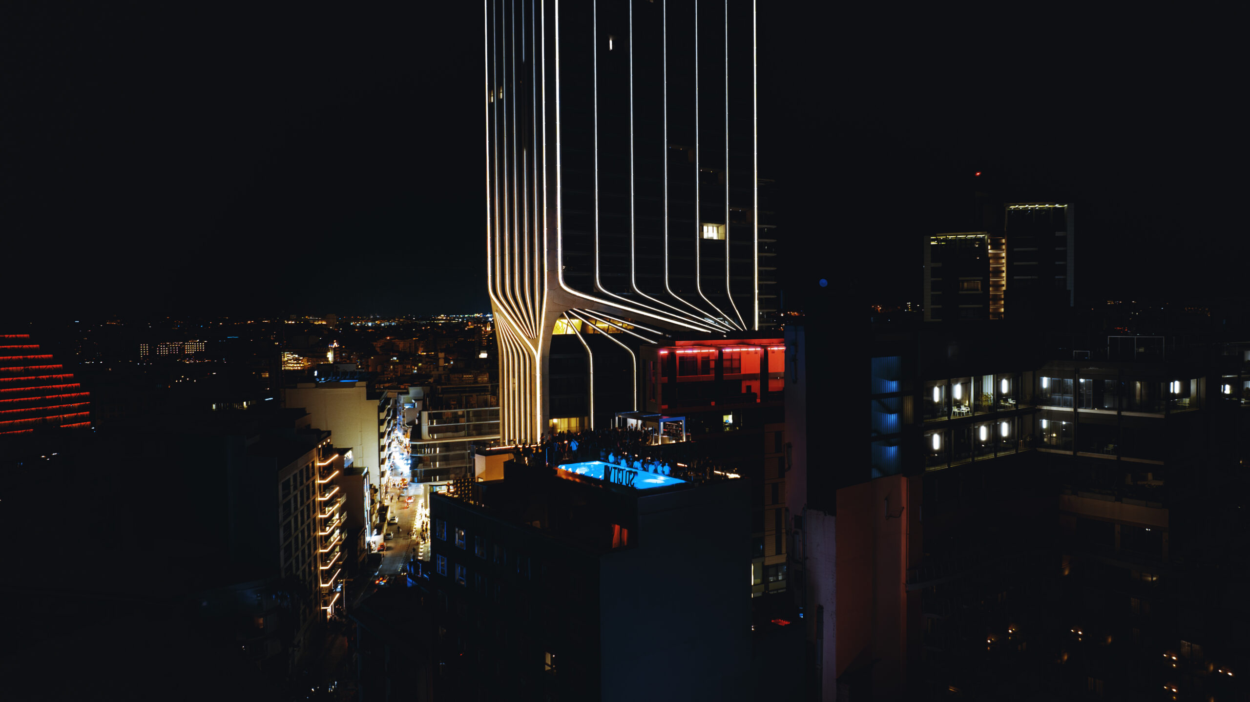 Night view of a lively rooftop with pool and glowing city buildings